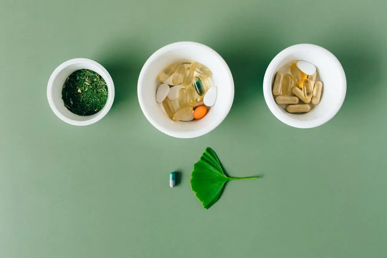 Vue de haut trois petits bols blancs avec spiruline et compléments alimentaires dedans posés sur fond vert avec une feuille verte et une gélule devant