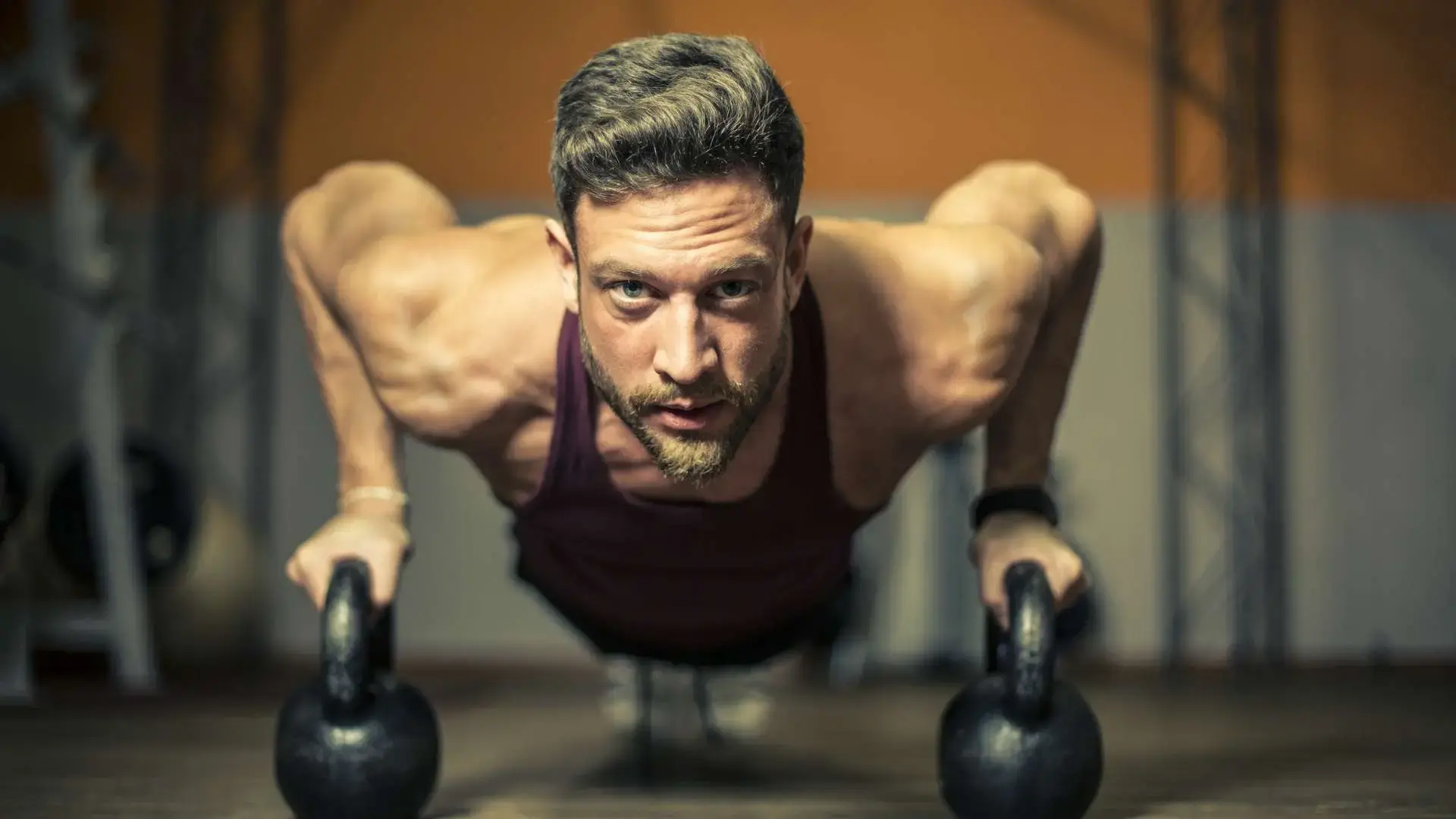 Homme de face en position pompes qui tient des poids en regardant devant lui